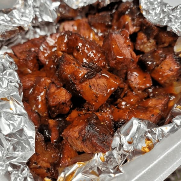 Close-up of glistening, saucy BBQ burnt ends in a foil-lined container from Uncle John's BBQ.