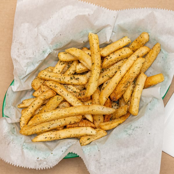 A green basket filled with golden French fries seasoned with herbs and spices, lined with white paper.