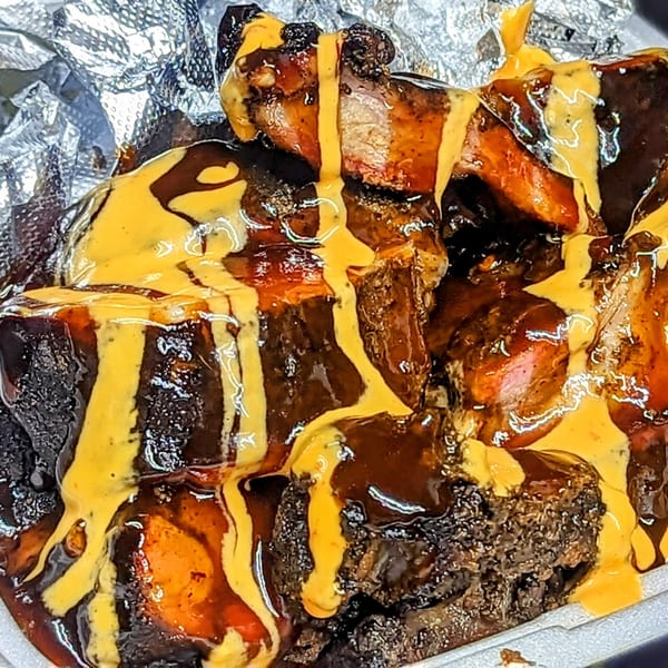 Close-up of Uncle John's BBQ ribs and burnt ends, generously drizzled with barbecue sauce and mustard.